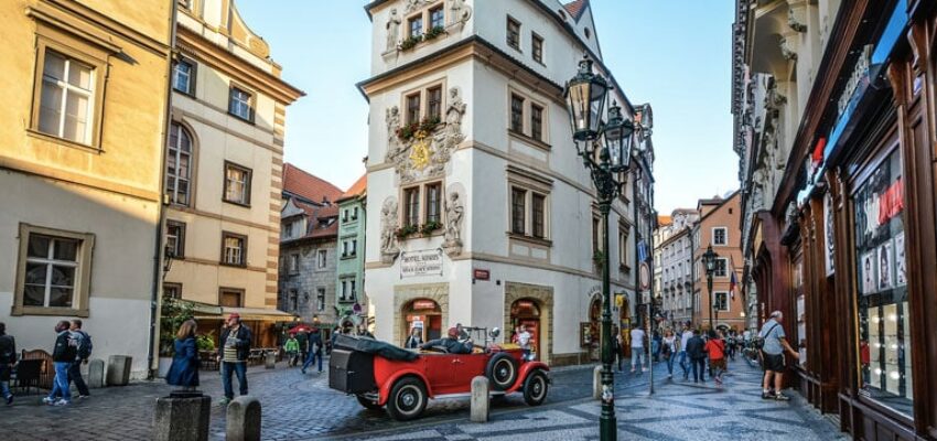Scène de rue historique, bâtiments, piétons, voiture vintage rouge.