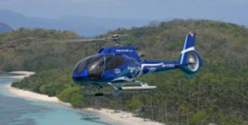 Hubschrauber mieten: hélicoptère survolant plage tropicale.